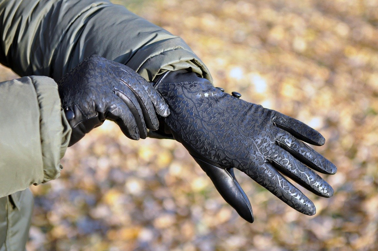 Person wearing elegant black leather gloves with a floral pattern, adjusting them outdoors in a park setting.

